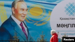 Kazakhstan -- A woman walks past a poster depicting Kazakh President Nursultan Nazarbaev in Almaty, February 16, 2015