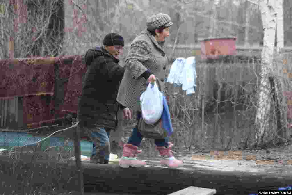 Есік алдындағы судан үйге кіріп шығу қиындаған. Төселген көпір үстінен өтіп бара жатқан әйелге ер адам жердемдесіп тұр.